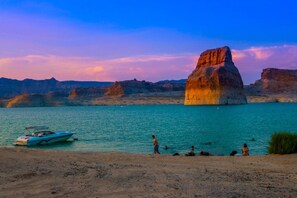 A lake with a large rock formation, a boat, and people on the shore.