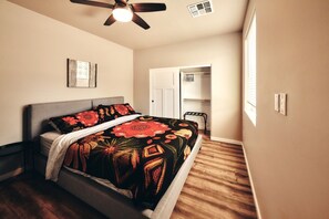 A bedroom with a bed, a ceiling fan, a wardrobe, and a door leading to another room.