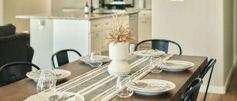 A dining table set with plates, glasses, and cutlery, a vase with dried plants, and a striped table runner.