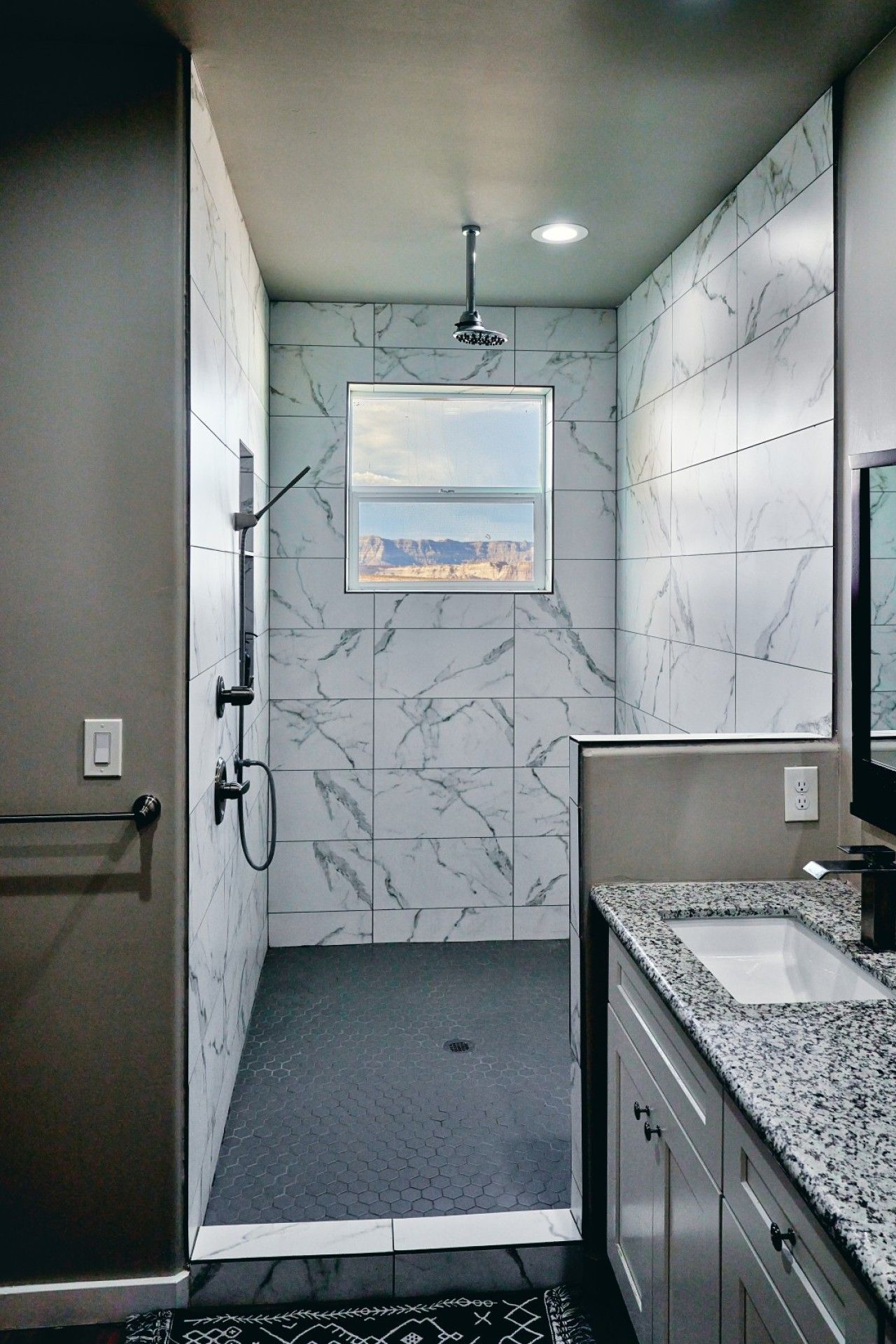 Ein modernes Badezimmer mit Dusche, Waschbecken und einem Fenster mit Bergblick.