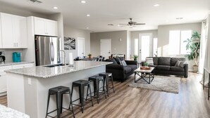 Una cocina moderna con una isla central, taburetes de bar, un refrigerador y un comedor con un sofá y una mesa de centro.