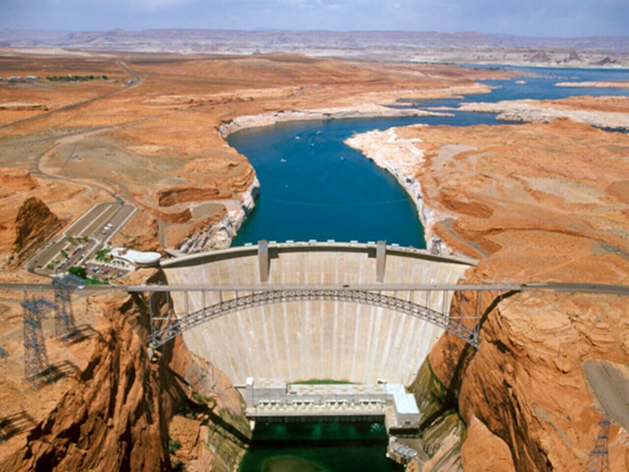 A large dam with a reservoir, a road leading to it, and a bridge crossing the reservoir.