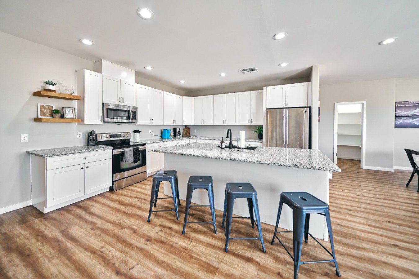 A modern kitchen with white cabinets, stainless steel appliances, a granite countertop, and bar stools.