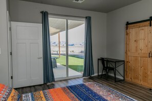 A room with a sliding glass door to a balcony, a wooden wardrobe, a small table, and a patterned rug.