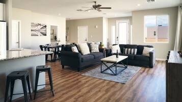 A spacious living area with a dark-colored sofa set, a coffee table, and a dining area with chairs and a table.