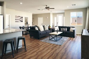 A spacious living area with a dark-colored sofa set, a coffee table, and a dining area with chairs and a table.