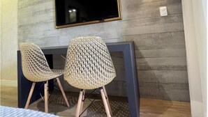 A room with a TV mounted on a wall, two wicker chairs, a dark-colored table, and a light switch. - View 462 just for you! (Plano Piloto)