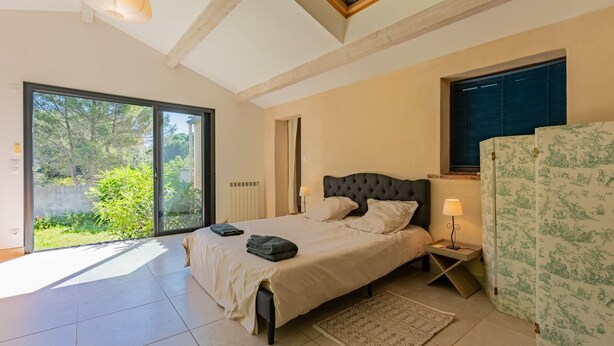 A bedroom with a bed, a bedside table, a lamp, a window, and a view of greenery outside. - Le Mas des Trois Sources - Grand jardin (Gignac)
