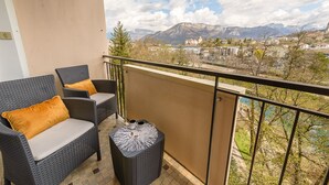 Un balcon doté de meubles en osier et d’une table, offrant une vue sur un paysage montagneux parsemé de bâtiments.