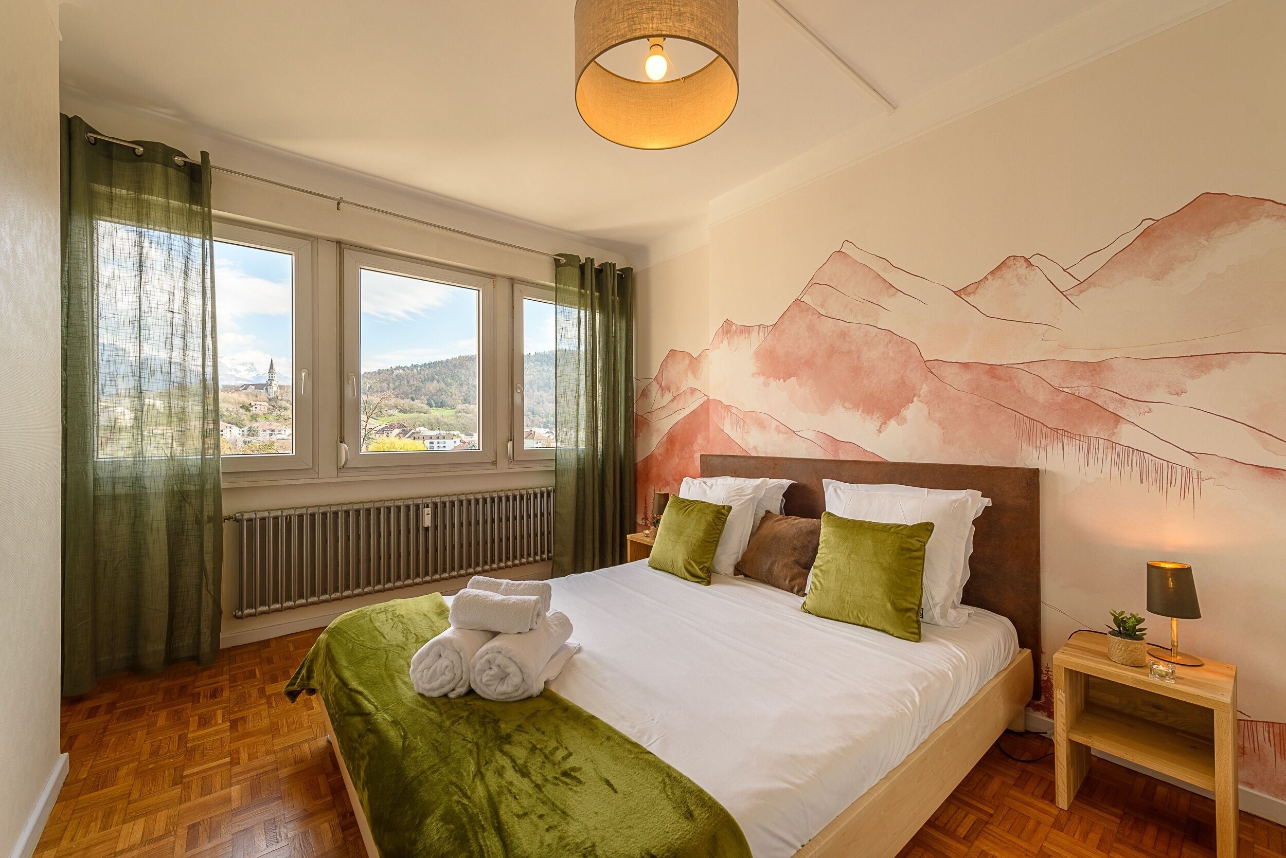 A bedroom with a large bed, a view of the outdoors, a radiator, and a lamp on a bedside table.