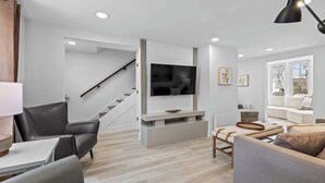 A modern living room with a flat-screen TV, a staircase, a sofa, a coffee table, and a lamp. - Spacious 3 Bdrm Haven - Steps to Downtown Ch'town (Charlottetown)