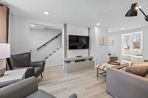 A modern living room with a flat-screen TV, a staircase, a sofa, a coffee table, and a lamp. - Spacious 3 Bdrm Haven - Steps to Downtown Ch'town (Charlottetown)