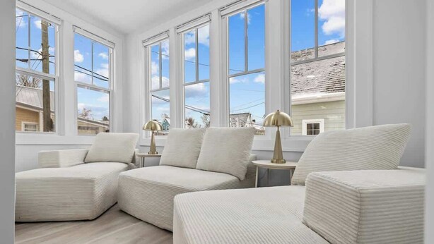 A room with large windows, a light-colored sofa set, and a small round table with a lamp. - Spacious 3 Bdrm Haven - Steps to Downtown Ch'town (Charlottetown)