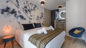 Ein modernes Schlafzimmer mit einem großen Bett, einem blauen Sessel, einem Wandspiegel und einem kleinen Nachttisch.