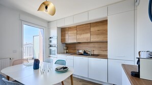 Una cucina moderna con mobili bianchi, zoccolo in legno e zona pranzo con tavolo bianco e sedie blu.