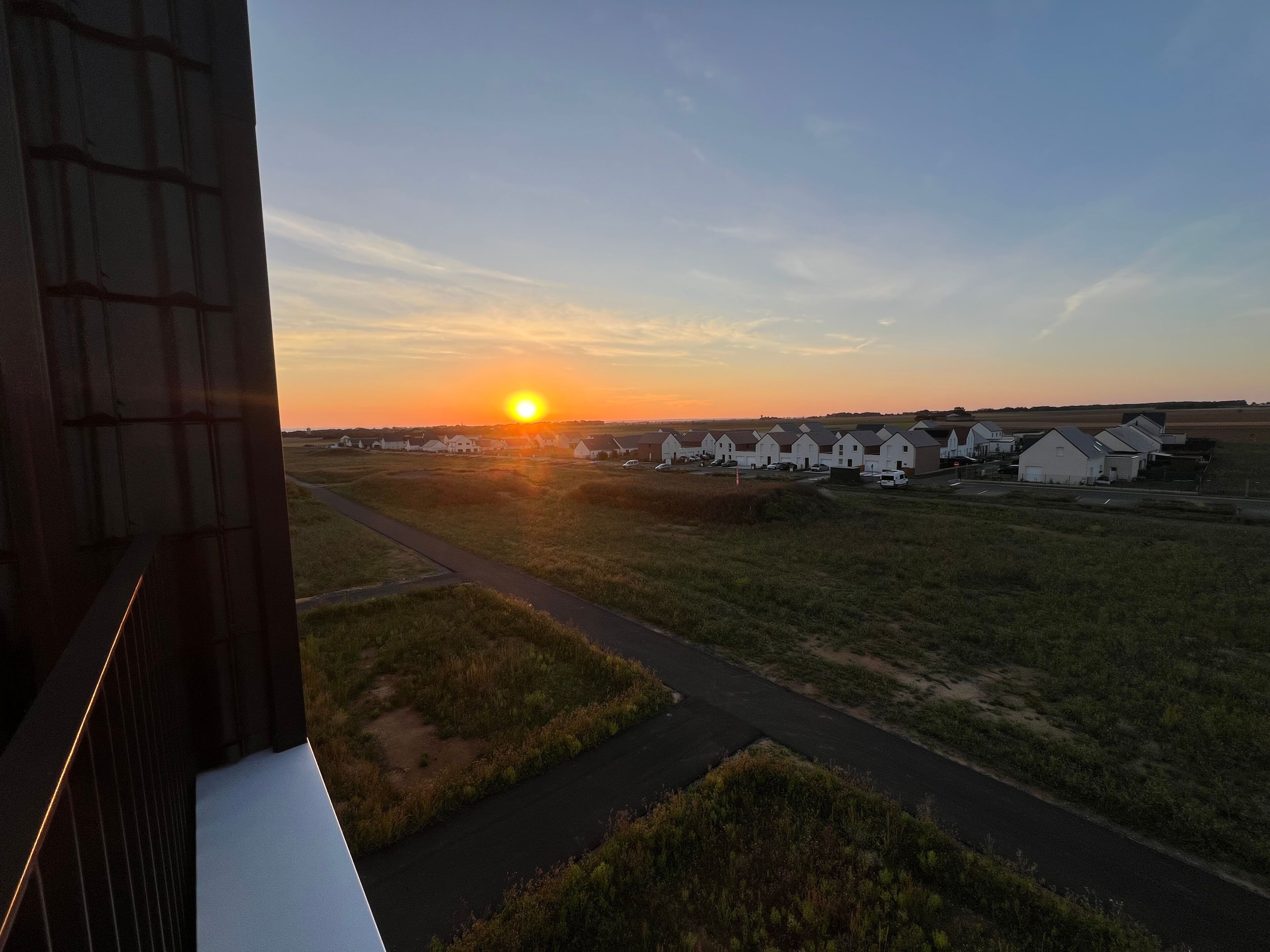 Een zonsondergang boven een woonwijk met huizen en een weg.