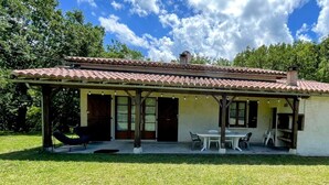A single-story house with a tiled roof, a covered patio with a table and chairs, and a lawn. - L'Oasis de SaBen - Piscine Privée (Belfort-du-Quercy)