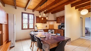 A modern kitchen with wooden beams, a dining table set for four, and a large window. - L'Oasis de SaBen - Piscine Privée (Belfort-du-Quercy)