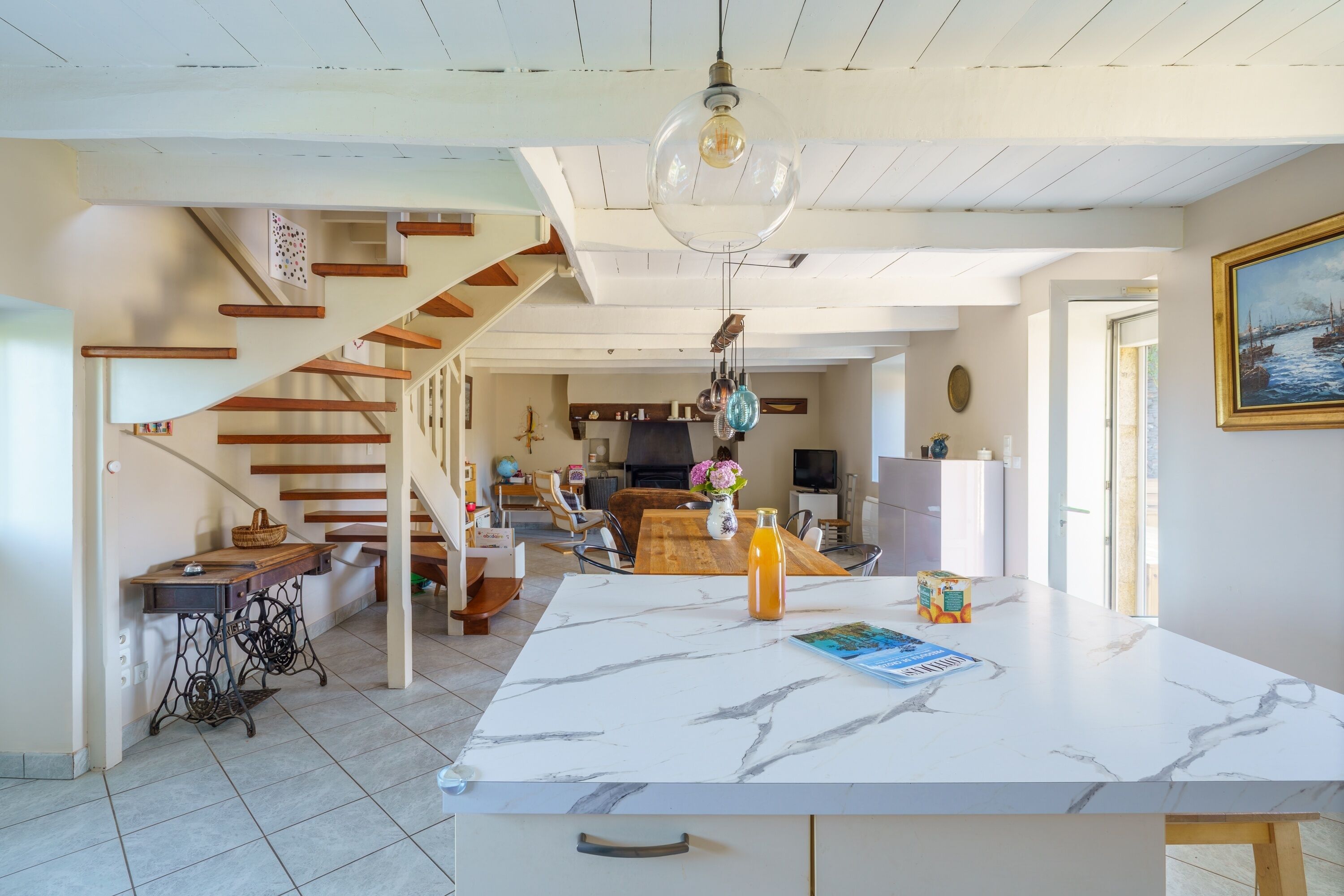 Una cocina amplia con encimera de mármol, una escalera de madera y un comedor con mesa y sillas.