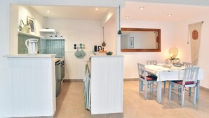 A dining area with a table set for four, a kitchen with white cabinetry, and a hanging light fixture. - Le Petit Carrelet - 10min de Dinan (Saint-Samson-sur-Rance)
