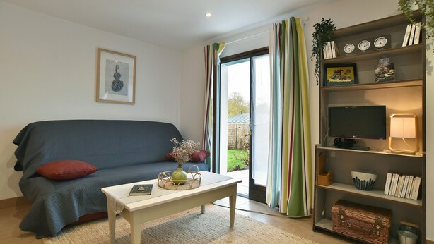 A living room with a sofa, a coffee table, a TV on a stand, and a bookshelf. - Le Petit Carrelet - 10min de Dinan (Saint-Samson-sur-Rance)