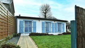 A small, single-story building with a white exterior and blue shutters, a paved pathway, and a grassy yard. - Le Petit Carrelet - 10min de Dinan (Saint-Samson-sur-Rance)