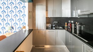 A modern kitchen with stainless steel appliances, a black countertop, and grey cabinets. - Grands Boulevards Home (Paris)