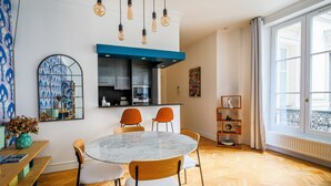A modern kitchen with a blue accent wall, a round marble table, and orange chairs. - Grands Boulevards Home (Paris)