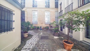 A courtyard with stone flooring, potted plants, and a building with multiple windows and balconies. - Saint Michel Seine Loft (Paris)