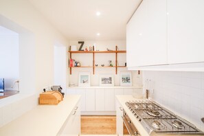 Eine moderne Küche mit weißen Schränken, einem Holzregal mit gerahmten Bildern und einem Gasherd.