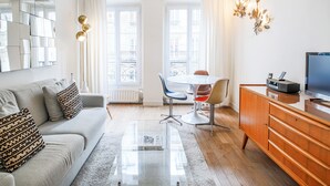 Een moderne woonkamer met een bank, een glazen salontafel, een eethoek met tafel en stoelen, en een tv op een houten kast.