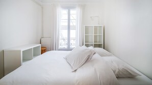 Een minimalistische slaapkamer met een bed, een wit wandrek en een radiator.