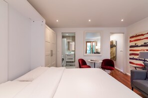 Quarto de hotel moderno com uma cama grande, uma mesa pequena, duas cadeiras e um quadro na parede.