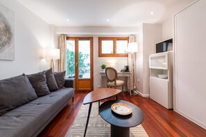 Ein modernes Wohnzimmer mit Sofa, Esstisch, Fernseher und Küchenbereich mit Kühlschrank und Schränken.