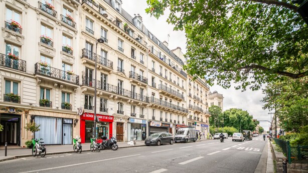 Eine Straße mit Gebäuden, einem roten Laden und geparkten Fahrzeugen.