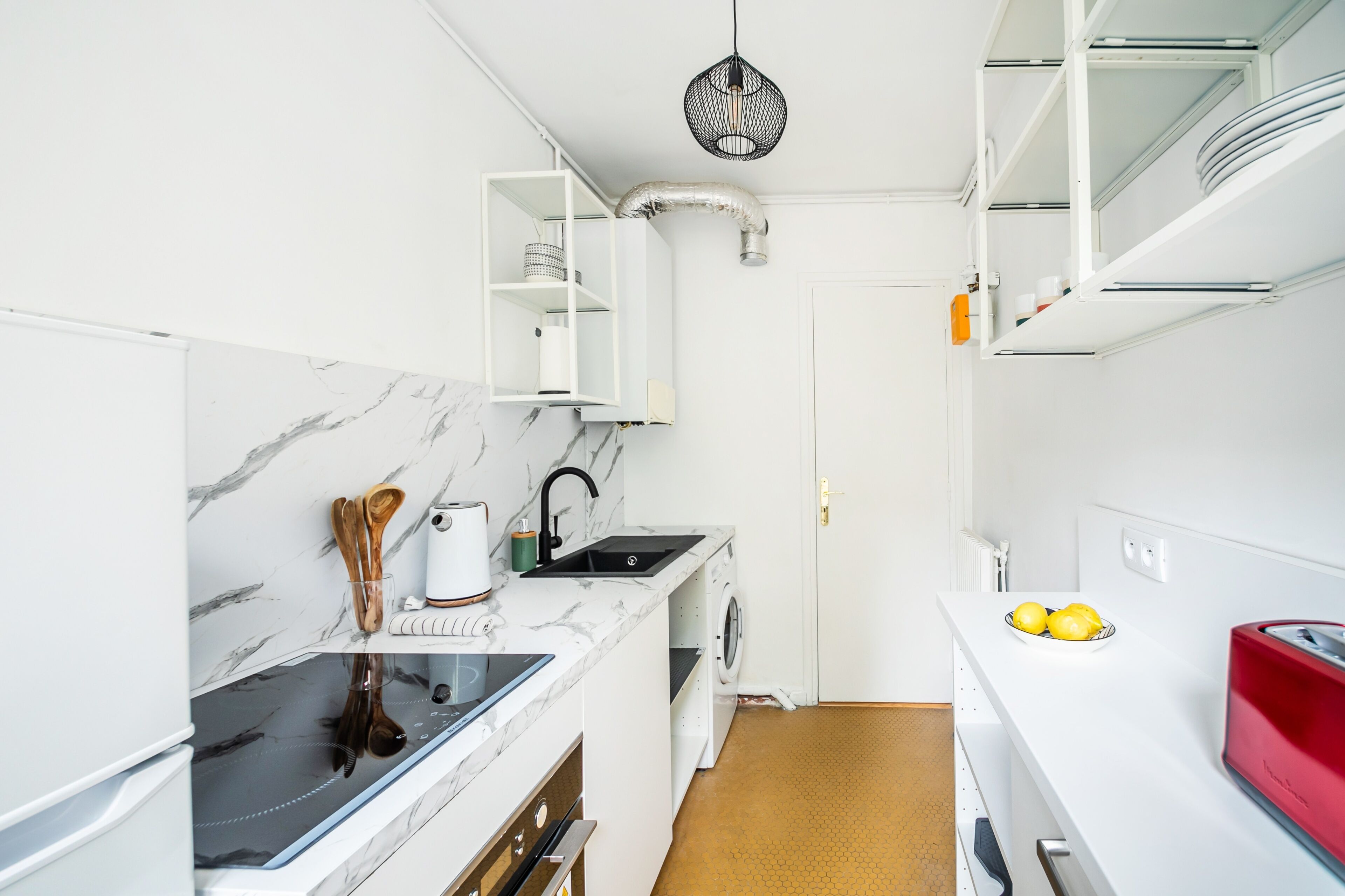 Een kleine keuken met witte kasten, een marmeren aanrechtblad, een inbouwoven, een spoelbak en een rode toaster.