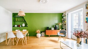 A modern living room with a green accent wall, wooden flooring, a dining table with chairs, a coffee table, a bookshelf, and a radiator. - Bonne Nouvelle Cosy - One Bedroom Apartment, Sleeps 2 (Paris)