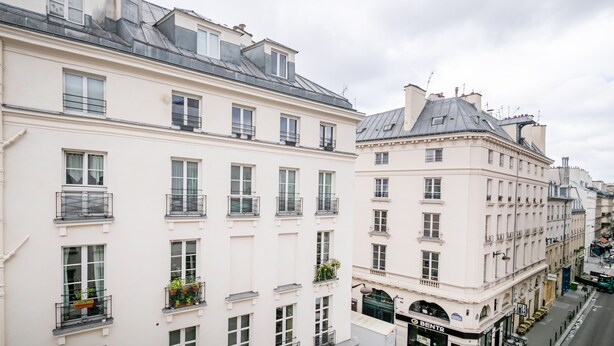 A row of white buildings with multiple windows and balconies, a street in front, and a clear sky. - Bonne Nouvelle Cosy - One Bedroom Apartment, Sleeps 2 (Paris)