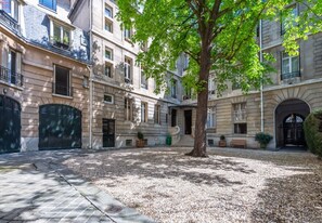 Un patio con un árbol, un edificio con múltiples ventanas y una entrada portonada.