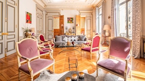 A spacious room with a sofa set, armchairs, a coffee table, and a chandelier.