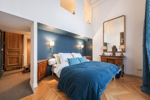 Un dormitorio con cama, mesitas de noche, cómoda, espejo y puerta.