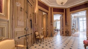 A grand hallway with ornate wooden doors, a chandelier, and a checkered floor.