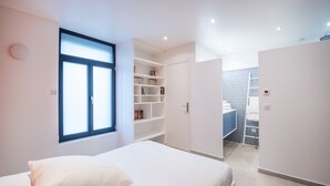 A modern bedroom with a bed, built-in shelving, and a view of a bathroom. - Tour Eiffel Loft - One Bedroom Apartment, Sleeps 3 (Paris)