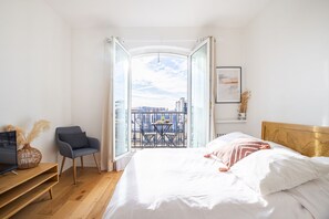 Ein Schlafzimmer mit Bett, Sessel, Fernseher und einem Balkon mit Tisch und Stühlen.