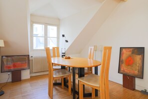 Ein Essbereich mit rundem Tisch und vier Stühlen, ein Fenster mit Jalousien, ein Heizkörper und ein gerahmtes Kunstwerk an der Wand.