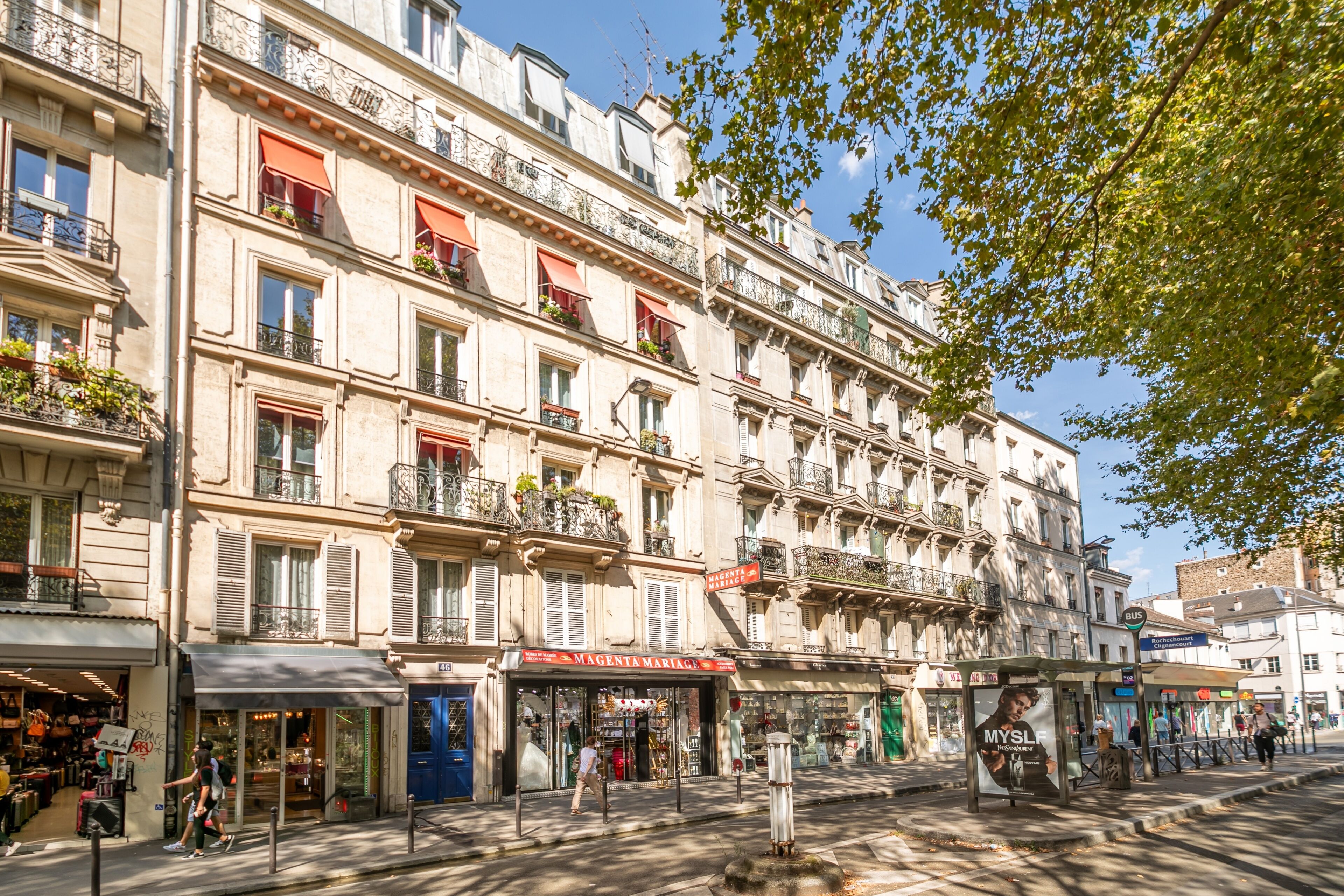 A multi-story building with balconies, storefronts, and a bus stop.