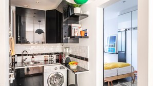 Una cocina compacta con lavadora, un lavabo, una encimera y una lámpara colgante verde.