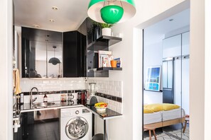 Eine kleine Küche mit Waschmaschine, Spüle, Arbeitsplatte und einer grünen Pendelleuchte.