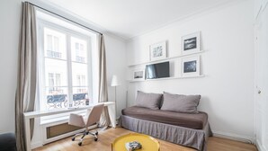 A room with a bed, a desk, a chair, a small table, and a window with curtains. - Alma Tour Eiffel - One Bedroom Apartment, Sleeps 3 (Paris)