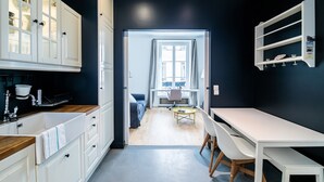 A modern kitchen with white cabinetry, a dining area with a white table and chairs, and a view through a doorway to a living room. - Alma Tour Eiffel - One Bedroom Apartment, Sleeps 3 (Paris)